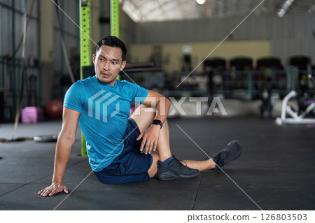 Fitness and Recovery. Man in a seated position on gym floor, preparing for stretching. 126803503