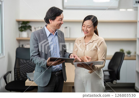 Team Collaboration and Document Sharing. Businessman and businesswoman discussing documents in a modern office. 126803530