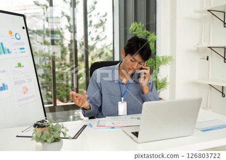 Professional Analyzing Financial Charts While on Phone Call in Office 126803722