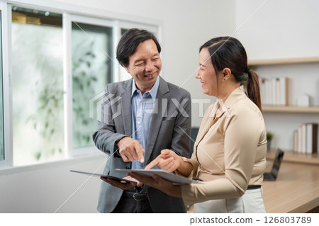 Professional Interaction and Document Review. Businessman and businesswoman sharing insights in a modern office. Professional Interaction and Document Review. Businessman and businesswoman sharing insights in a modern office. 126803789