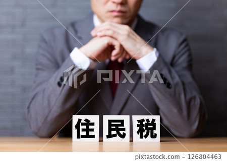 A middle-aged male businessman wearing a suit and worrying about resident tax blocks 126804463