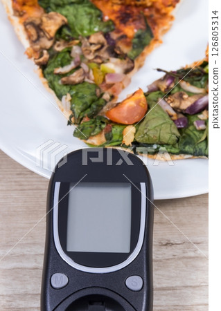 Glucometer for checking sugar level and fresh baked vegetarian pizza. Nutrition during diabetes Glucometer for checking sugar level and fresh baked vegetarian pizza. Nutrition during diabetes 126805314