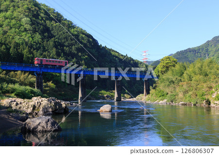 Nagaragawa Railway diesel railcar running along the clear waters of the Nagaragawa River 126806307
