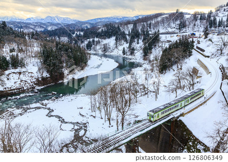 A diesel train on the Iiyama Line crosses the Sakae Ohashi Bridge, with snow still remaining on the Chikuma River. 126806349