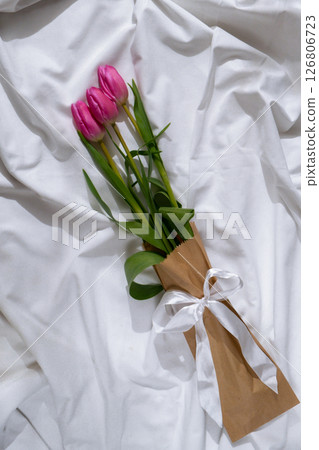 Bouquet of pink tulips in craft eco-friendly paper bag on messy bed. Romantic morning scene. Greeting card Holiday flowers springtime 126806723