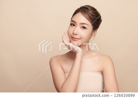 A beautiful young Asian woman with clean, fresh skin against a beige background. Skincare, facial treatment, cosmetology, beauty, and spa. An elegant portrait of an Asian woman. 126810899