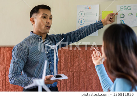 ESG Discussion on Renewable Energy. Male presenter explaining wind turbine concepts to a female colleague. ESG Discussion on Renewable Energy. Male presenter explaining wind turbine concepts to a female colleague. 126811936