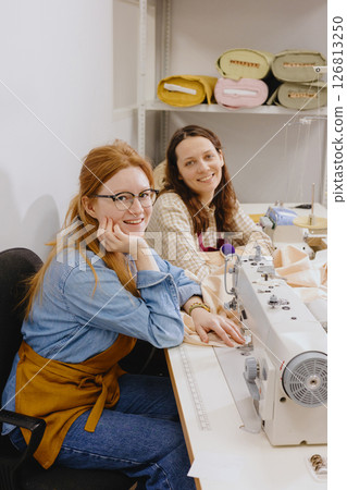 Two female seamstresses in the workshop at the factory are working at tables on sewing machines.  126813250