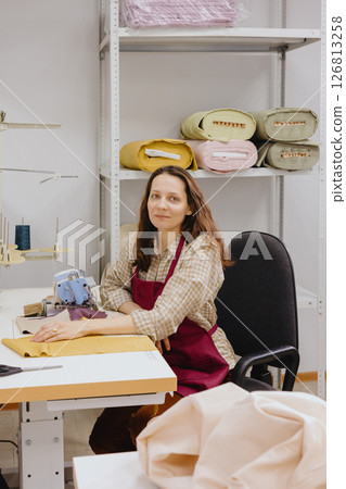 happy woman fashion designer seamstress is sitting at a sewing machine at work. 126813258