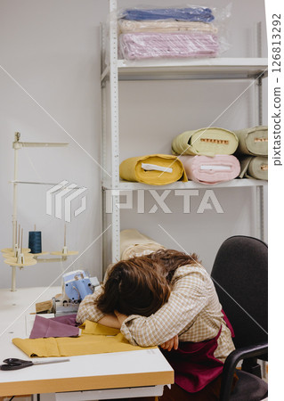 Sad woman fashion designer seamstress sits at sewing machine head clones, overtime. 126813292
