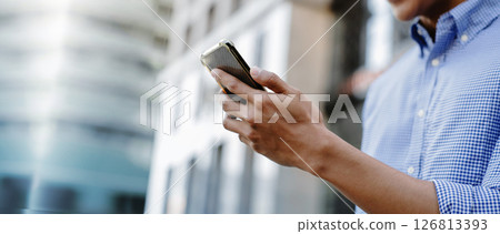 A man using a smartphone in an urban environment, representing mobile communication, digital lifestyle, and business on the go 126813393