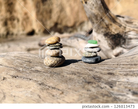 stacked stones on driftwood near sandy beach during bright sunlight showcase nature's art. closeup. stacked stones on driftwood near sandy beach during bright sunlight showcase nature's art. closeup. 126813473