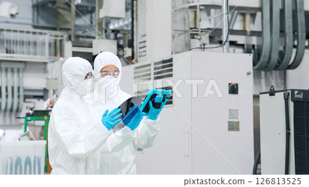 Male and female workers in protective clothing inspecting silicon wafers with a tablet in a semiconductor factory Male and female workers in protective clothing inspecting silicon wafers with a tablet in a semiconductor factory 126813525
