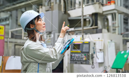A female worker inspecting factory machinery with a tablet 126813538