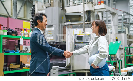 A male business person and a female worker shaking hands in a factory A male business person and a female worker shaking hands in a factory 126813539