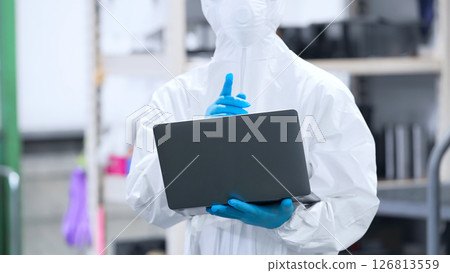 Worker in protective clothing using laptop in factory Worker in protective clothing using laptop in factory 126813559