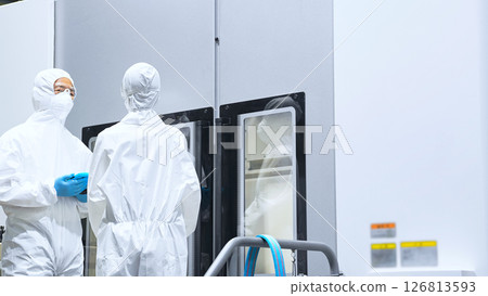 Male and female workers in protective clothing operating factory machines 126813593