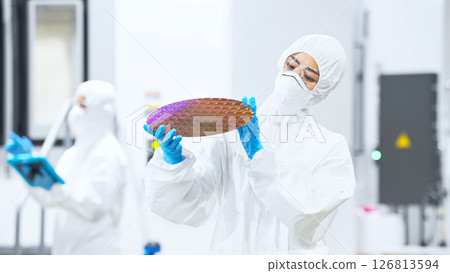 一名身穿防護服的女工在半導體工廠檢查矽片 一名身穿防護服的女工在半導體工廠檢查矽片 126813594