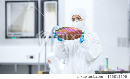 一名身穿防護服的女工在半導體工廠檢查矽片 一名身穿防護服的女工在半導體工廠檢查矽片 126813596