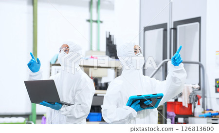 Male and female workers wearing protective clothing working in a factory with digital devices Male and female workers wearing protective clothing working in a factory with digital devices 126813600