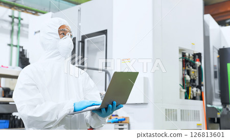 A male worker wearing protective clothing working in a factory with a laptop 126813601