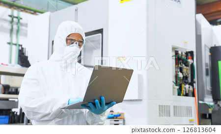 A male worker wearing protective clothing working in a factory with a laptop 126813604