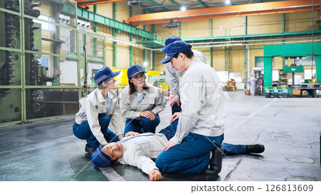 A group of people providing medical assistance to a worker who collapsed at a factory 126813609