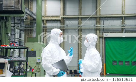 Male and female workers wearing protective clothing talking in a factory 126813631