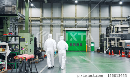 Back view of male and female workers wearing protective clothing walking through a factory 126813633