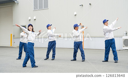 A group of workers doing exercises in front of a factory 126813648