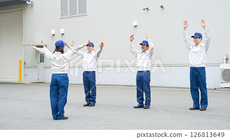 A group of workers doing exercises in front of a factory 126813649