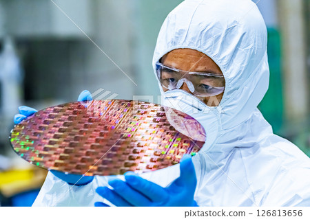 Male worker in protective clothing inspecting silicon wafers in a semiconductor factory 126813656
