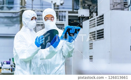 Male and female workers in protective clothing inspecting silicon wafers while looking at a tablet in a semiconductor factory Male and female workers in protective clothing inspecting silicon wafers while looking at a tablet in a semiconductor factory 126813661