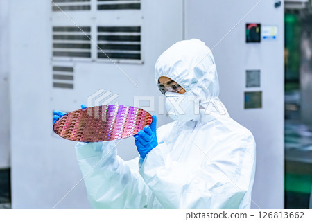 A female worker in protective clothing inspects silicon wafers in a semiconductor factory A female worker in protective clothing inspects silicon wafers in a semiconductor factory 126813662
