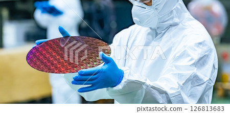 一名身穿防護裝備的工人在半導體工廠檢查矽片 126813683