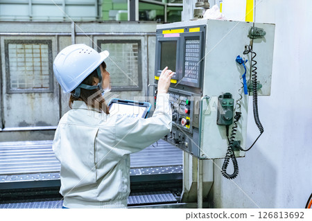 A female worker operates a factory machine with a tablet 126813692