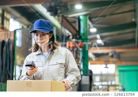 A group of female workers using handheld terminals to manage products in a factory 126813704