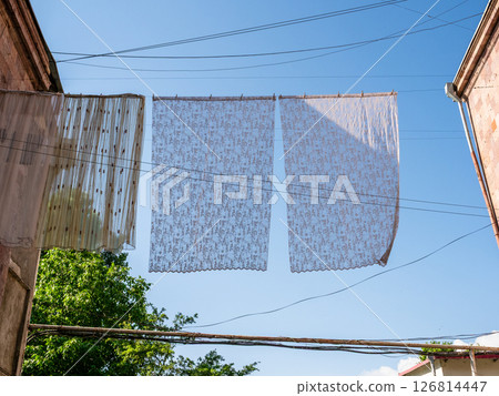 tulle curtains dry on clothesline between houses tulle curtains dry on clothesline between houses 126814447