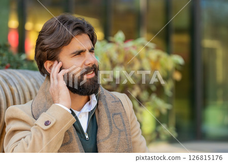 Indian young business man suffers from earache, ear pain, infection, inflammation on city street Indian young business man suffers from earache, ear pain, infection, inflammation on city street 126815176