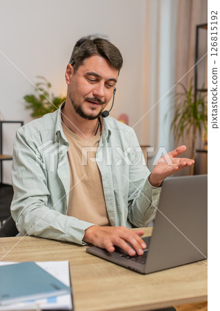 Young male customer service representative with headset using laptop computer at home office table 126815192