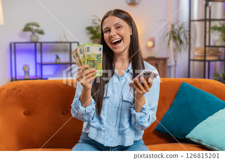Smiling happy rich young woman counting money euro cash use smartphone, income, saves, lottery win Smiling happy rich young woman counting money euro cash use smartphone, income, saves, lottery win 126815201
