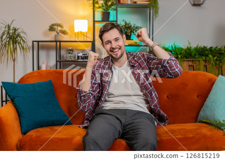 Happy Caucasian man watching TV shouting celebrating success winning goal achievement good news Happy Caucasian man watching TV shouting celebrating success winning goal achievement good news 126815219