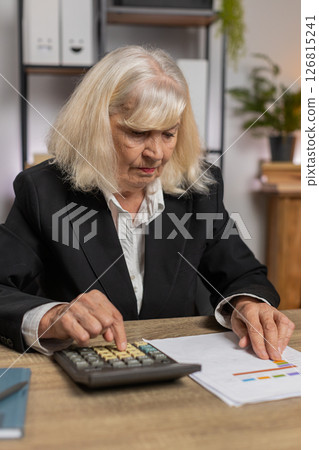 Upset senior businesswoman accountant doing calculation for financial report at home office desk Upset senior businesswoman accountant doing calculation for financial report at home office desk 126815241