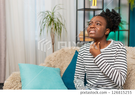 African American ill sick woman coughing, holding throat feeling sore throat pain indoors at home African American ill sick woman coughing, holding throat feeling sore throat pain indoors at home 126815255