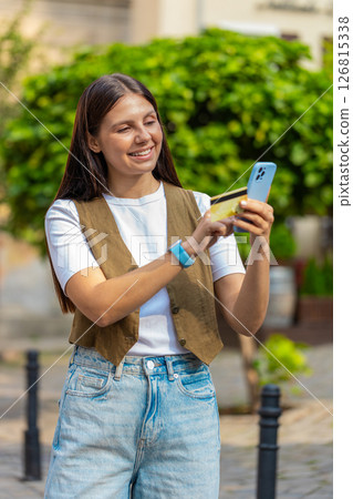 Happy Caucasian woman using credit card smartphone while purchases online shopping on city street 126815338