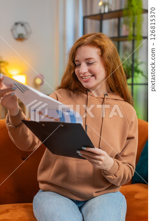 Woman accountant working with financial graph documents reading reports of income on sofa at home Woman accountant working with financial graph documents reading reports of income on sofa at home 126815370