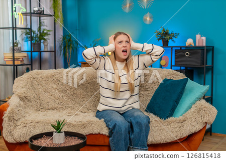 Caucasian woman irritated by noisy neighbors covering ears on sofa construction music loud indoors Caucasian woman irritated by noisy neighbors covering ears on sofa construction music loud indoors 126815418