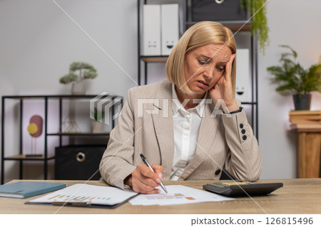 Upset mature businesswoman using calculator feeling worried about financial problem at office desk 126815496