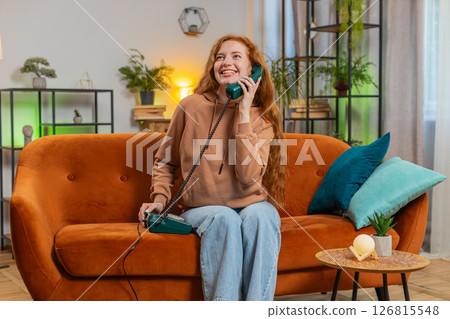 Smiling young woman making wired telephone call conversation with friends sitting on sofa at home 126815548