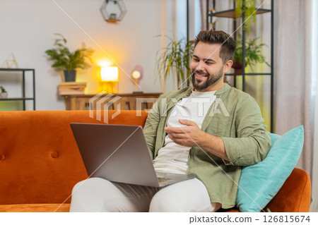 Confident young man on sofa couch using laptop making an online video conference call in distance 126815674